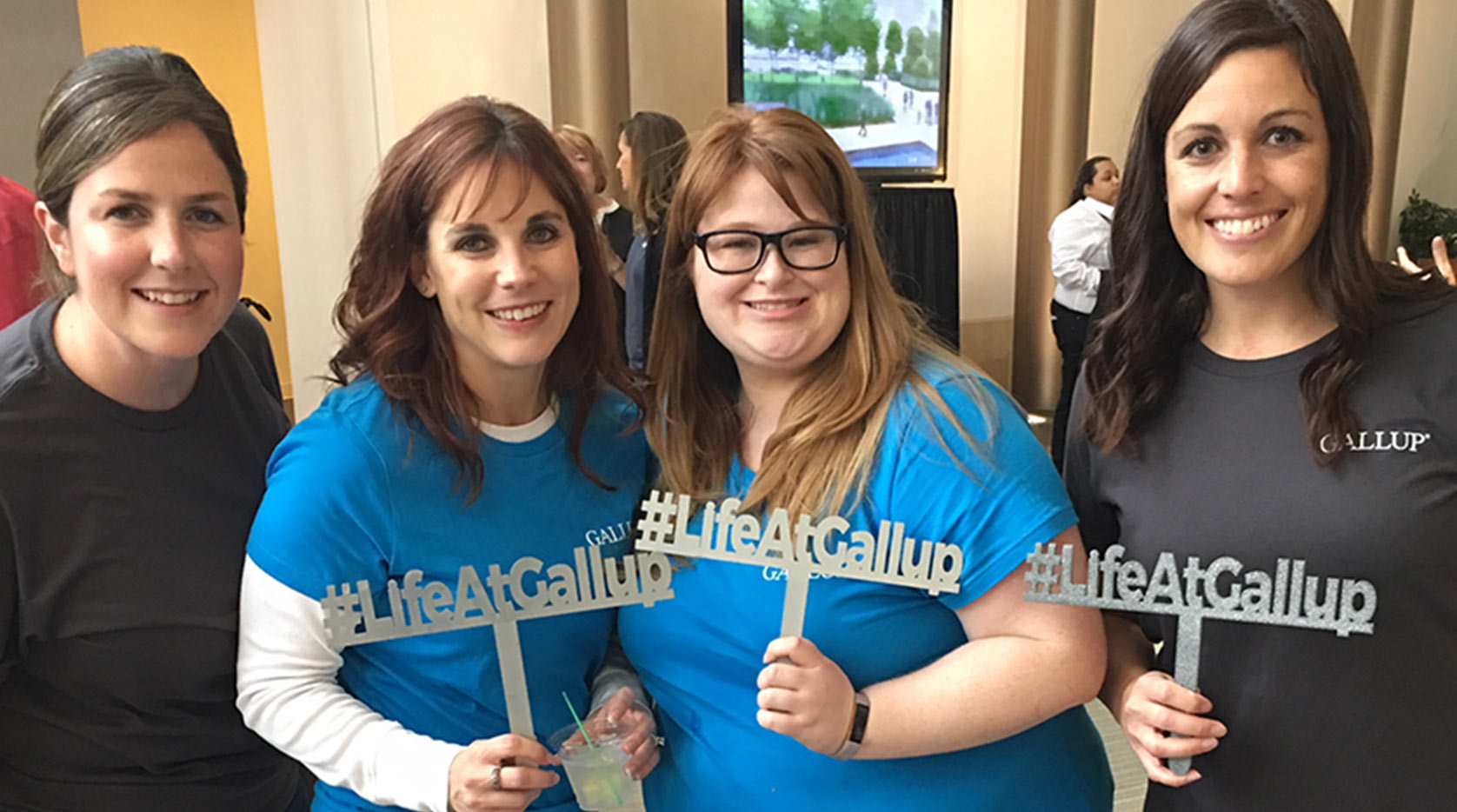 A group of four women employees with #LifeAtGallup signs.