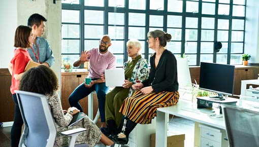 A group of mixed race coworkers gather together in a brightly lit office in a circle