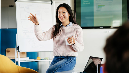 A smiling young woman speaks to a group in front of a whiteboard