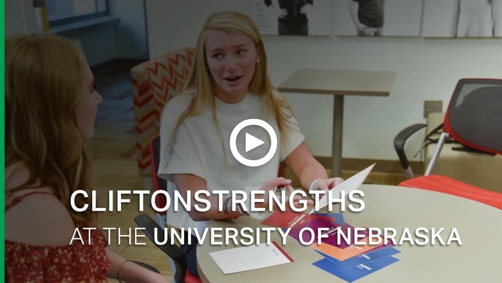 Video thumbnail: Two female students sit and talk at a round table. Overlaid text reads 'CliftonStrengths at the University of Nebraska' below a white play button.