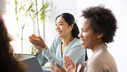 A group of women smile and clap around a table.