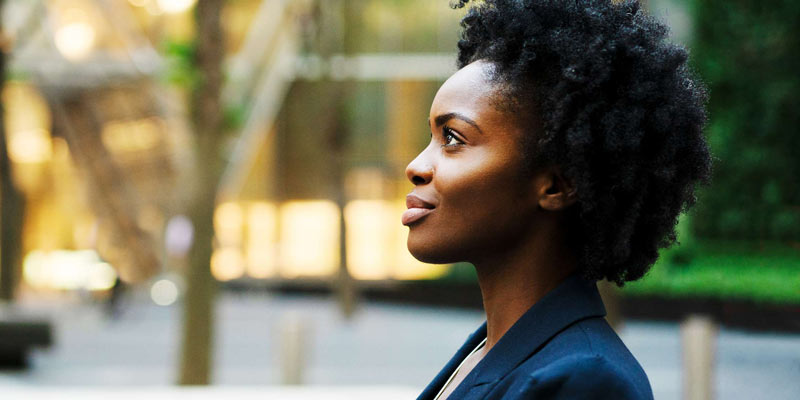 A young woman in a suit jacket smiles and looks up outside of a building