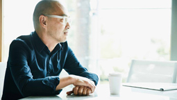 Middle Aged Asian man in glasses sits next to window at desk