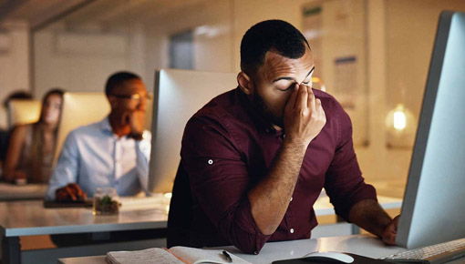 Man pinches the bridge of his nose in frustration at his desk