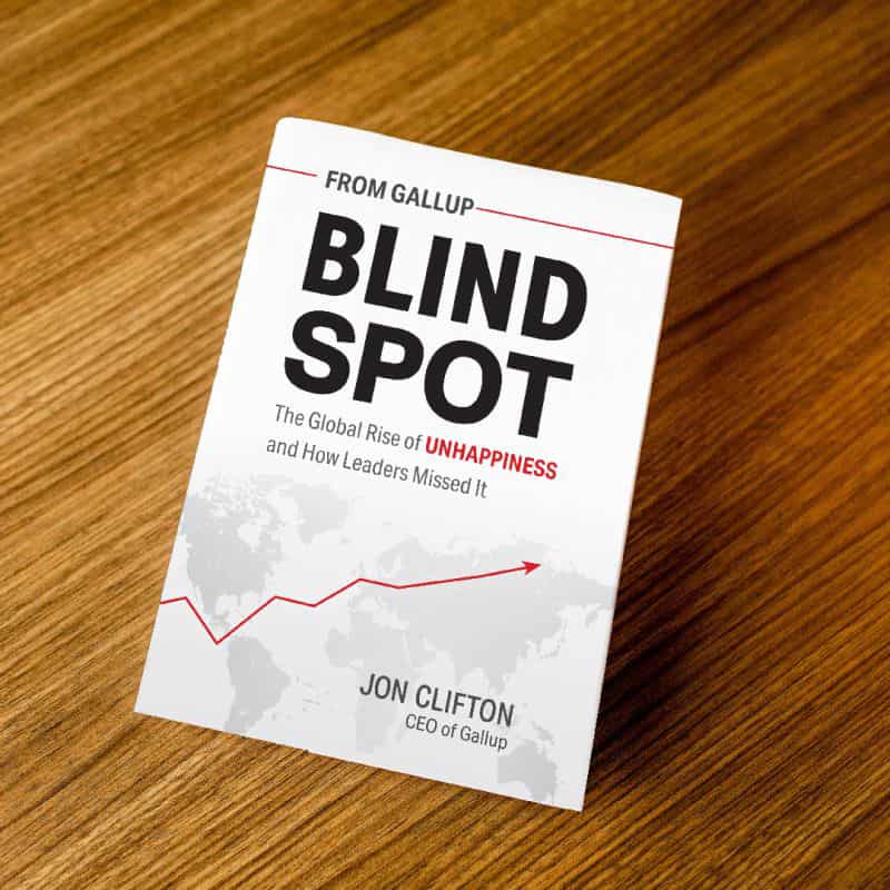 Cover of 'Blind Spot: The Global Rise of Unhappiness and How Leader Missed It' by Jon Clifton, CEO of Gallup, on a wood table top.