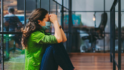 Woman sits on office floor, distressed, wearing face mask