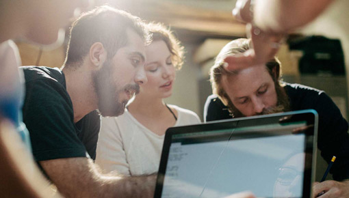 A group of employees gather to talk around a laptop