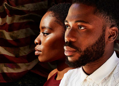 A somber looking Black man and woman in front of an American flag