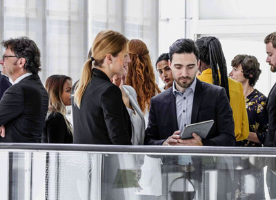 A man in a suit looks at a tablet computer in a crowd of people in business attire