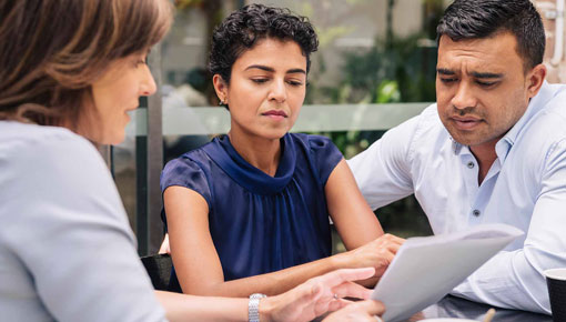 A woman discusses the information in a packet of papers with two customers in an office.