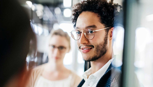 A smiling young man with glasses talks to his coworkers