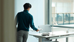 Male employee with short dark hair walks towards a desk with papers in hand