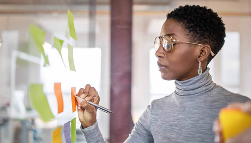 Young woman with glasses writes notes on bulletin board