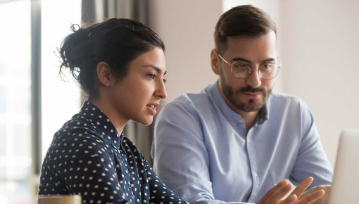 Two coworkers gather in front of a laptop computer to talk