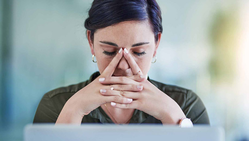 Young woman with dark hair rests head pensively in hands at a computer