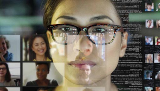 A young woman wearing glasses looks at a computer screen containing multiple open program windows