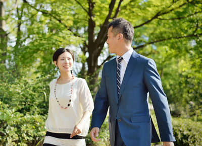 A man and a woman walking through a park with trees.