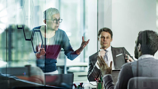 An older business woman gestures with her hands while presenting to colleagues