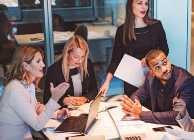 A group of coworkers gather around a laptop at a table