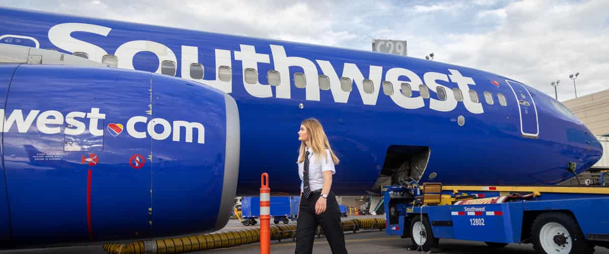 A female pilot walks in front of a bright blue Southwest Airlines jet plane.