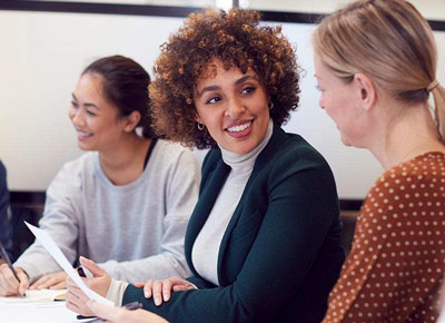 A smiling woman in business attire speaks to a coworker