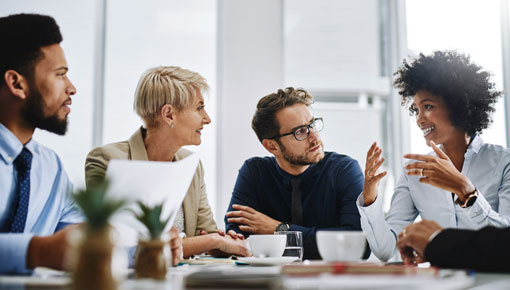 Three coworkers sit at a table and listen intently to a fourth coworker as she talks