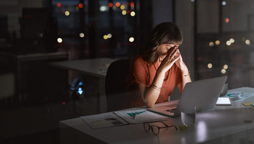 A woman presses her hands to her forehead in frustration while sitting in a dark office