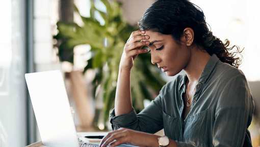 A young woman leans her forehed on her hand while working at a laptop computer