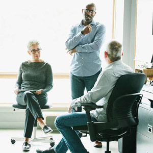 Three colleagues talk together at a desk in an office