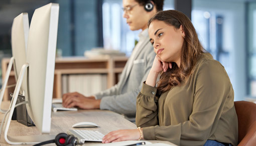 Two employees sitting side by side at their computers in an open workspace.