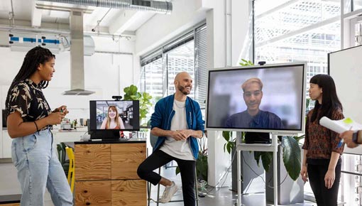 Three coworkers gather in an office with remote workers via video chat