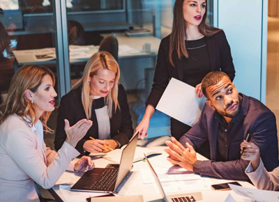 A group of colleagues talk together around a laptop at a table in an office