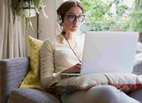 Young white woman with glasses sits on a window seat with a laptop