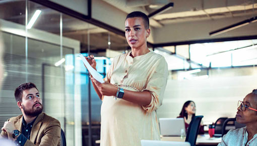 A pregnant woman speaks with papers in her hands to colleagues in an office