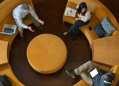 An overhead shot of three coworkers talking while seated at a round coffee table