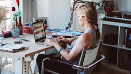 Young white woman works on laptop at desk in home office