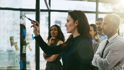 A woman writes on a whiteboard in front of colleagues in an office