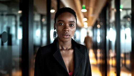 A young woman in a suit jacket looks serious in an office hallway