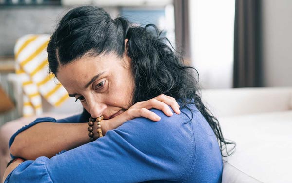 A woman looks down, sadly, while hugging her arms to her chest