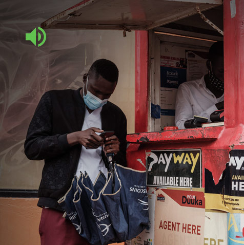 Man standing at a stall looking at a phone while holding a folded up umbrella.