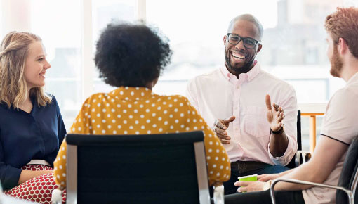 Two men and two women in business attire smiling and sitting around a table having a conversation.