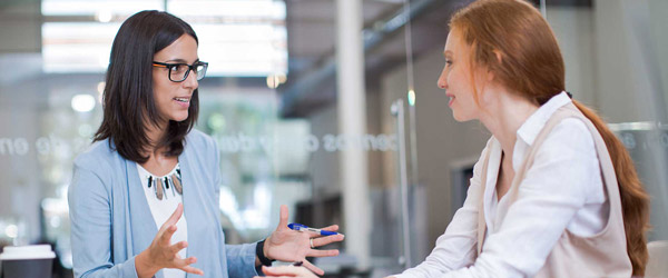 Two women talking in a glass conference room.