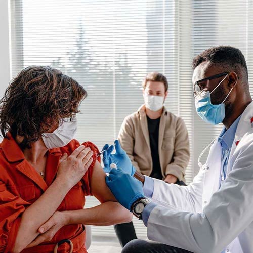 Doctor giving woman vaccination while an onlooker watches