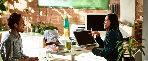 Woman talking to man visiting her at her desk.