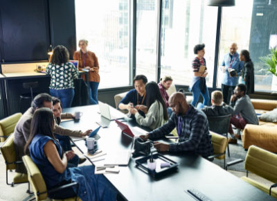 A group of 14 men and women in business attire split up into small groups in a coworking space.