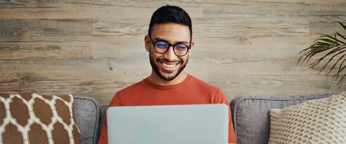 A smiling man with glasses types on a laptop computer.