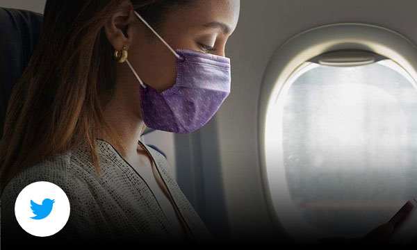 Woman on flight wearing mask and looking at phone.